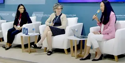 Three people sitting in chairs in front of a screen talking into microphones.