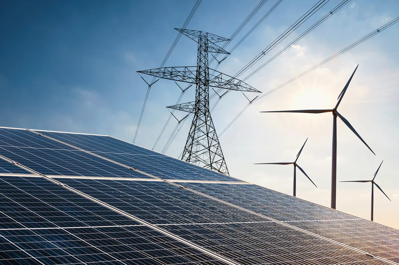Solar panels in the foreground with power lines and wind turbines against a blue sky in the background.