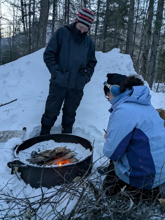 Two people start a small campfire while they are surrounded by snow.